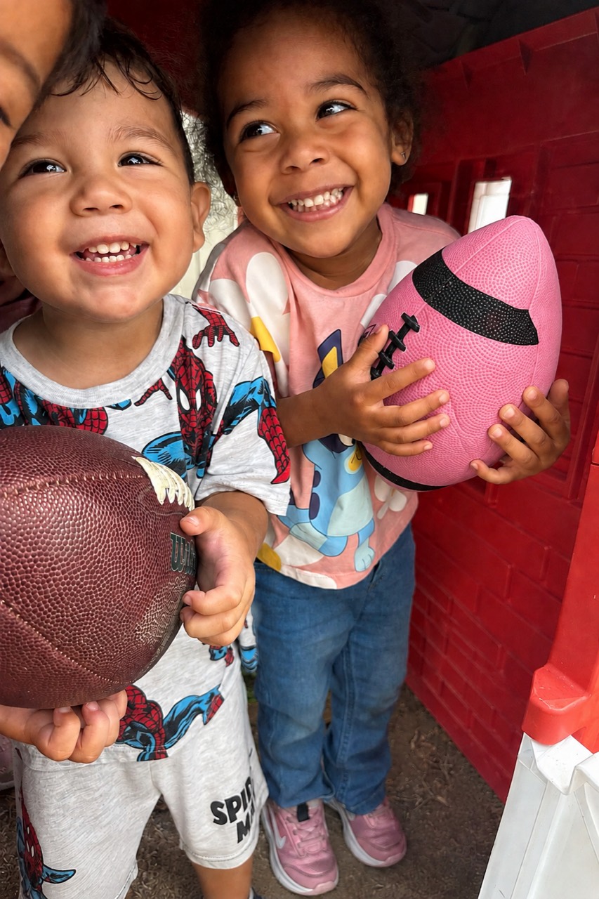 A boy and girl happily holding footballs during play at Little World Changers